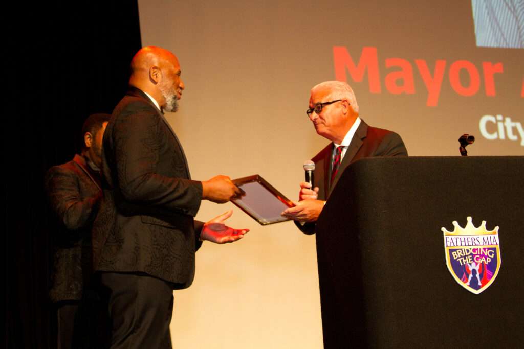 Two men in suits exchanging an award on stage.